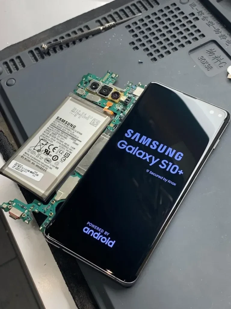 Disassembled Samsung Galaxy S10 Plus displaying startup screen beside internal battery